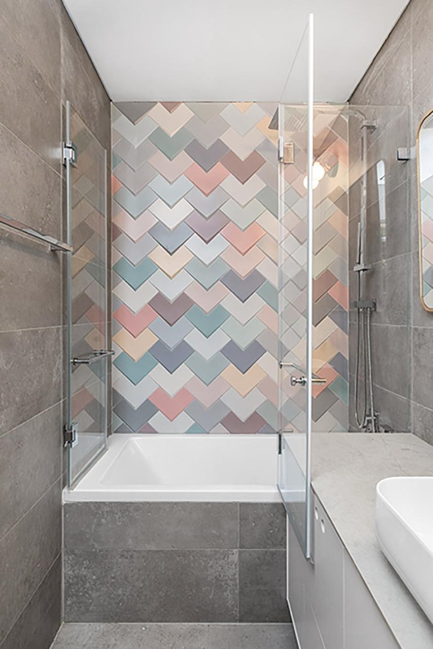 Designer bathroom with colorful chevron accent tiles, gray stone-look walls, built-in tub with glass partition, and white vessel sink
